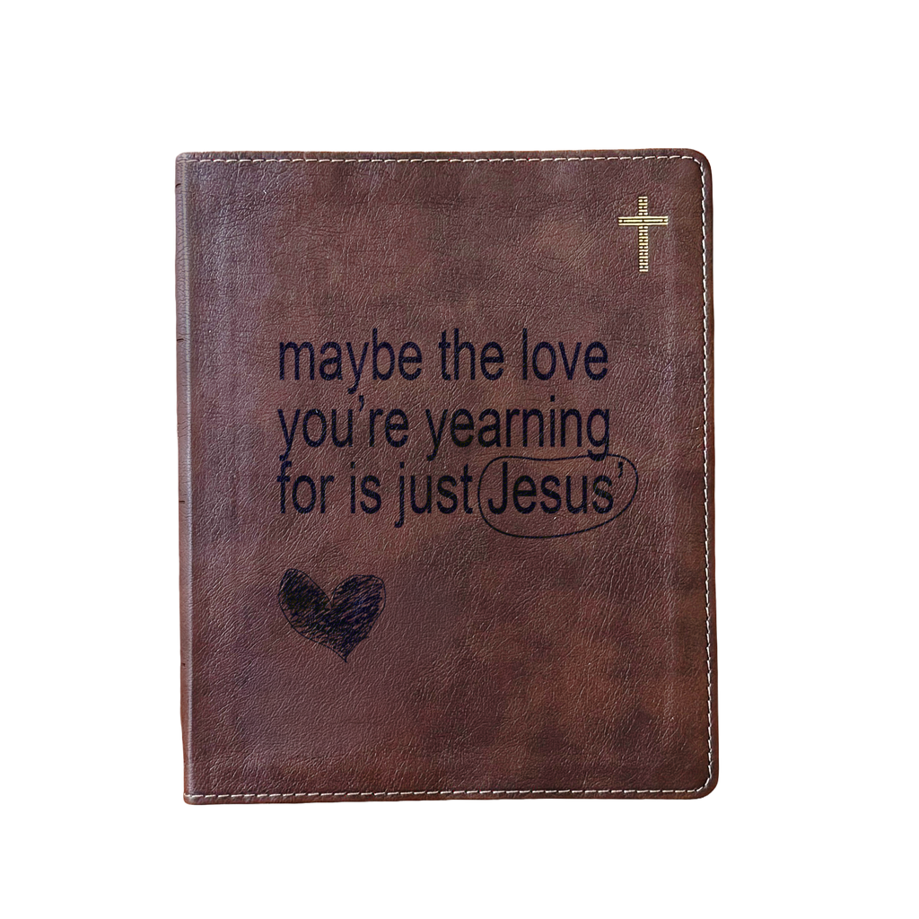 A brown faux-leather Bible cover or journal with a gold cross in the top right corner and the printed phrase 'maybe the love you're yearning for is just Jesus' with a heart and underline graphic on the front, shown on a plain white background.