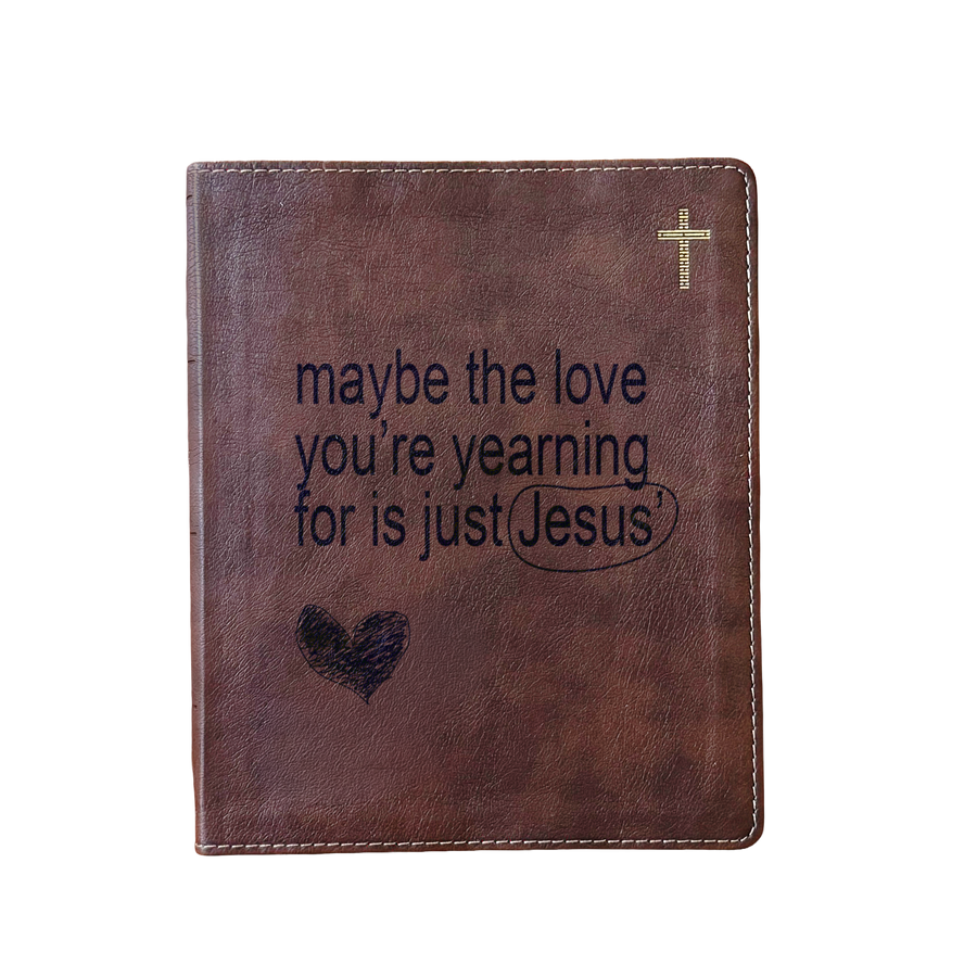 A brown faux-leather Bible cover or journal with a gold cross in the top right corner and the printed phrase 'maybe the love you're yearning for is just Jesus' with a heart and underline graphic on the front, shown on a plain white background.