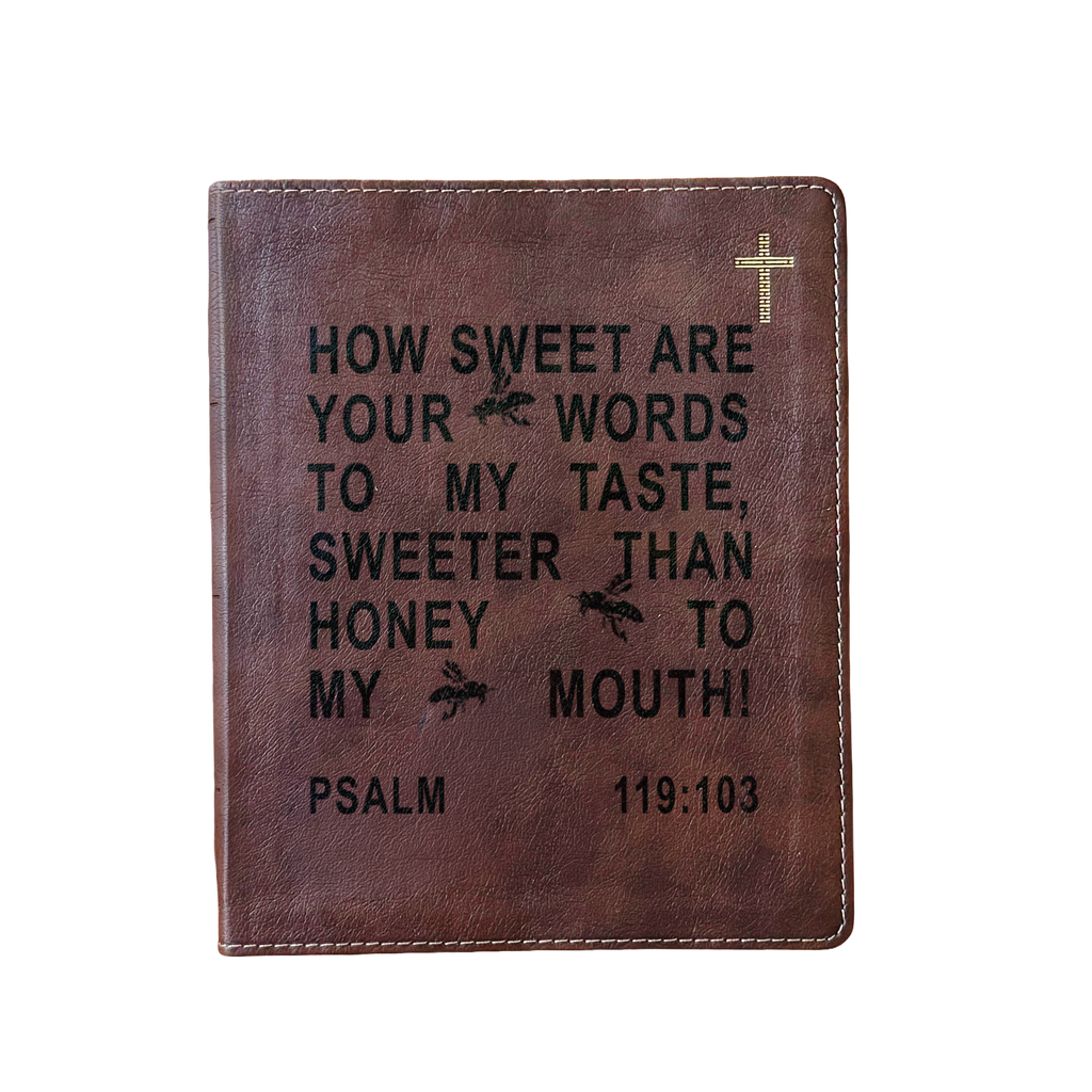 A brown leather Bible cover featuring black embossed text from Psalm 119:103 and a small gold cross in the top right corner, shown against a plain white background.