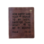 A brown leather Bible cover featuring black embossed text from Psalm 119:103 and a small gold cross in the top right corner, shown against a plain white background.