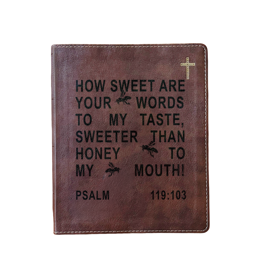 A brown leather Bible cover featuring black embossed text from Psalm 119:103 and a small gold cross in the top right corner, shown against a plain white background.