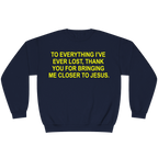 A navy blue crewneck sweatshirt with bold yellow text on the chest that reads, 'TO EVERYTHING I'VE EVER LOST, THANK YOU FOR BRINGING ME CLOSER TO JESUS.'.