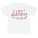 A white short-sleeve crewneck t-shirt featuring the text 'MY SOUL MAGNIFIES THE LORD!' printed on the chest in a textured, distressed pink font.