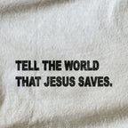 A close-up of a light beige or off-white fabric surface with bold black text reading, 'TELL THE WORLD THAT JESUS SAVES.'