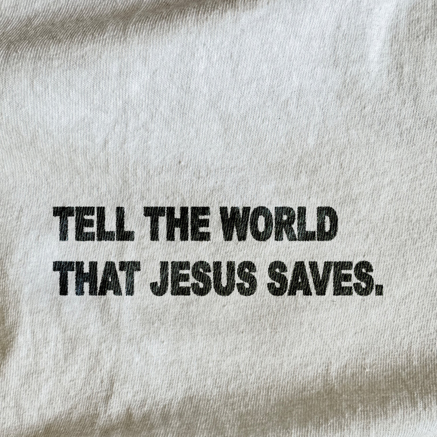 A close-up of a light beige or off-white fabric surface with bold black text reading, 'TELL THE WORLD THAT JESUS SAVES.'