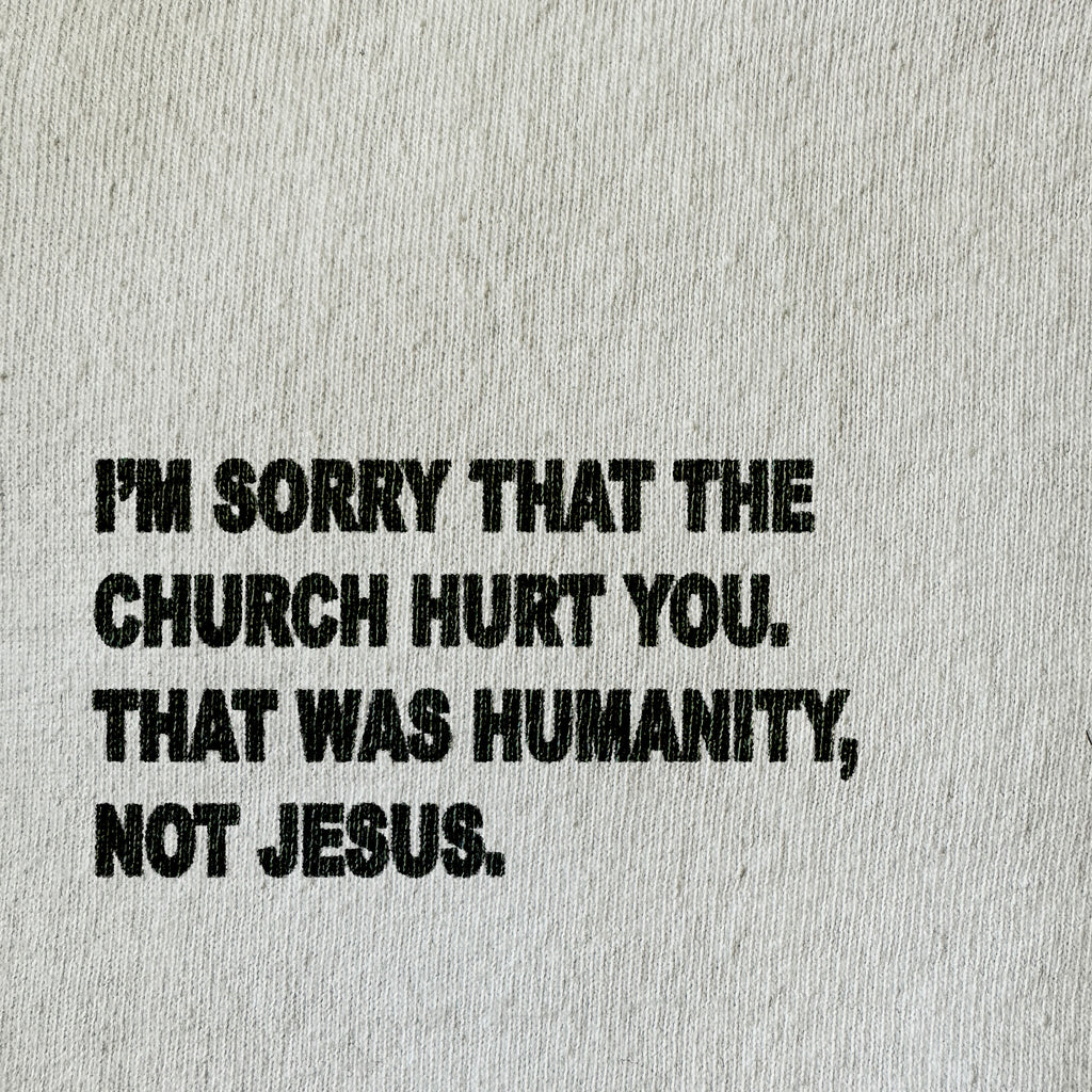 A close-up of a light beige textured fabric with bold black printed text that reads, 'I'M SORRY THAT THE CHURCH HURT YOU. THAT WAS HUMANITY, NOT JESUS.