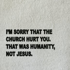 A close-up of a light beige textured fabric with bold black printed text that reads, 'I'M SORRY THAT THE CHURCH HURT YOU. THAT WAS HUMANITY, NOT JESUS.