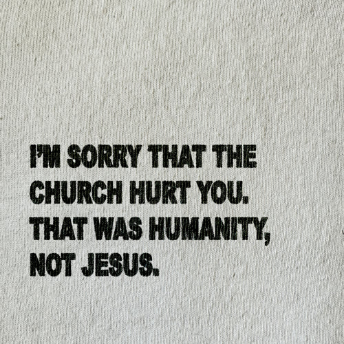 A close-up of a light beige textured fabric with bold black printed text that reads, 'I'M SORRY THAT THE CHURCH HURT YOU. THAT WAS HUMANITY, NOT JESUS.