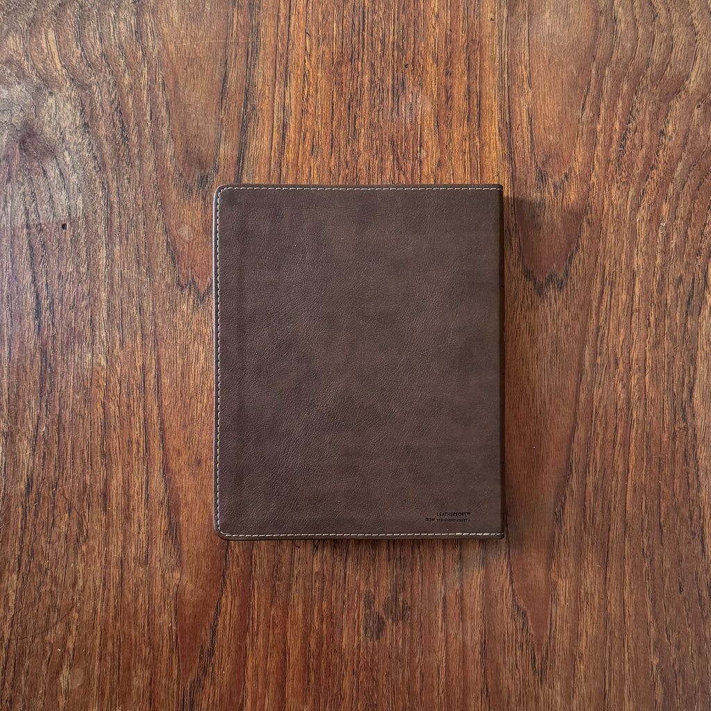 A dark brown leather notebook cover or tablet sleeve, shown closed from the front on a rustic wooden surface.