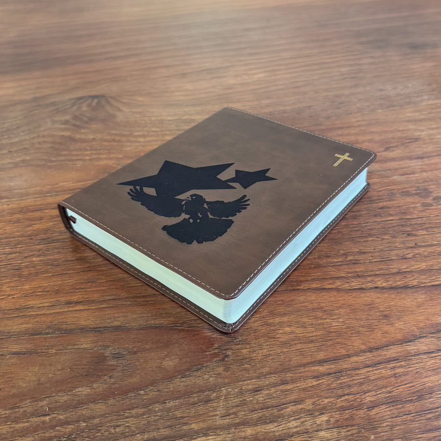 A brown leather-bound book with a black eagle and cross design on the cover, resting on a wooden tabletop.