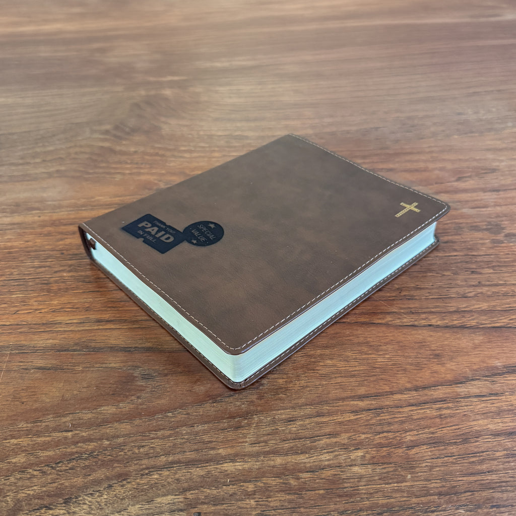 A brown leather-bound book with a gold cross on the cover, placed on a wooden table. A black and blue 'PAID' card is attached to the front cover.