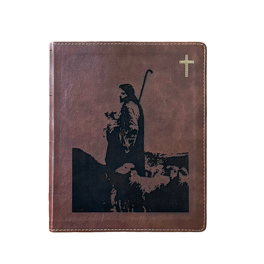 A brown leather-bound book or journal featuring a black silhouette graphic of a shepherd holding a staff, with a small gold cross in the upper right corner, shown on a plain white background.