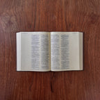 An open Bible with printed text on cream-colored pages, placed flat on a dark brown wooden surface.