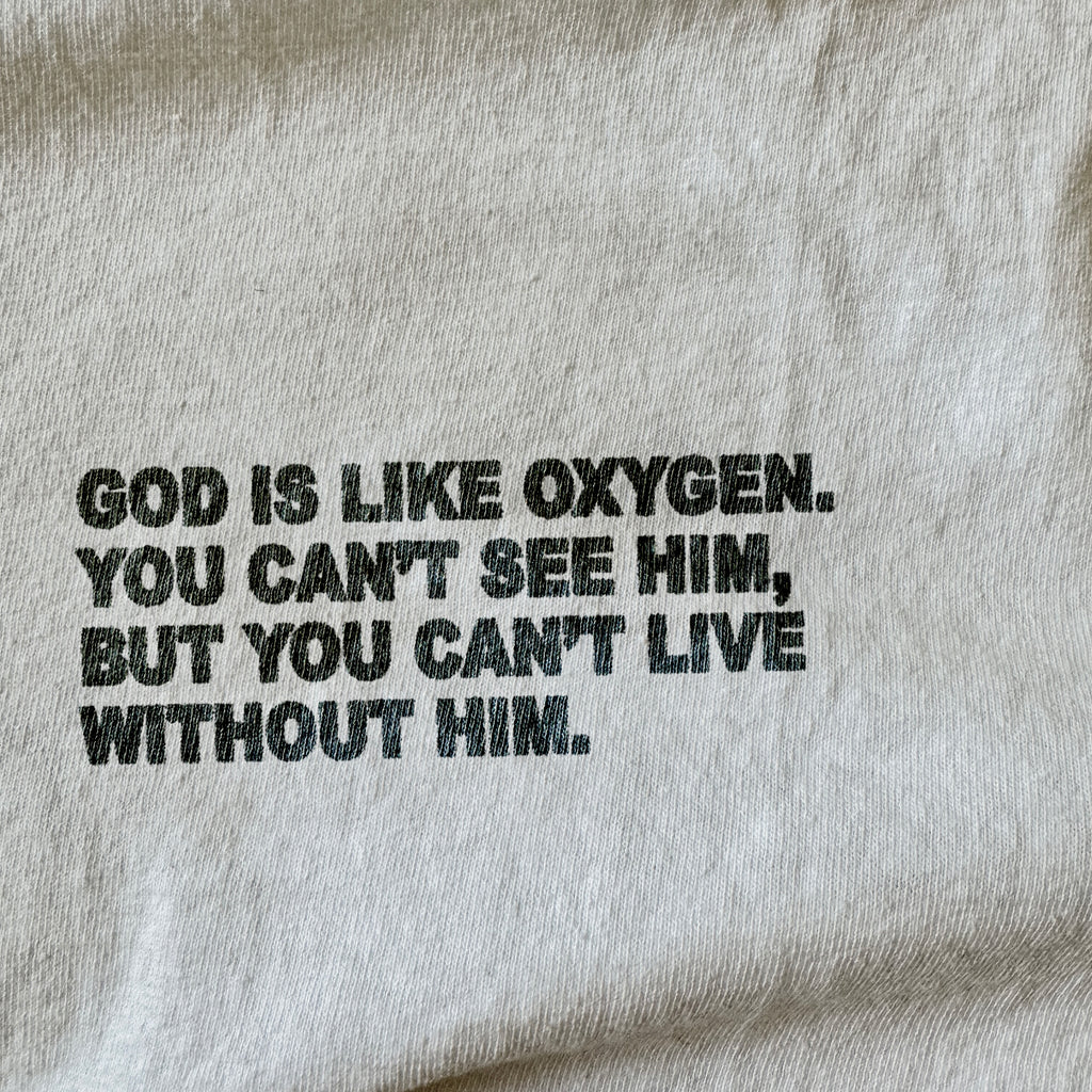 Close-up of a light beige fabric surface with black printed text reading, 'GOD IS LIKE OXYGEN. YOU CAN'T SEE HIM, BUT YOU CAN'T LIVE WITHOUT HIM.