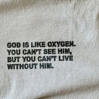 Close-up of a light beige fabric surface with black printed text reading, 'GOD IS LIKE OXYGEN. YOU CAN'T SEE HIM, BUT YOU CAN'T LIVE WITHOUT HIM.
