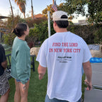 A man standing outdoors in a backyard wearing a white t-shirt with red and black text on the back reading 'FIND THE LORD IN NEW YORK CITY' and 'FOLLOW NOW'.