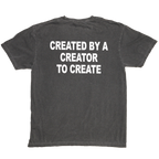 A dark gray washed t-shirt shown from the back, featuring the phrase 'CREATED BY A CREATOR TO CREATE' printed in bold white capital letters across the upper back.
