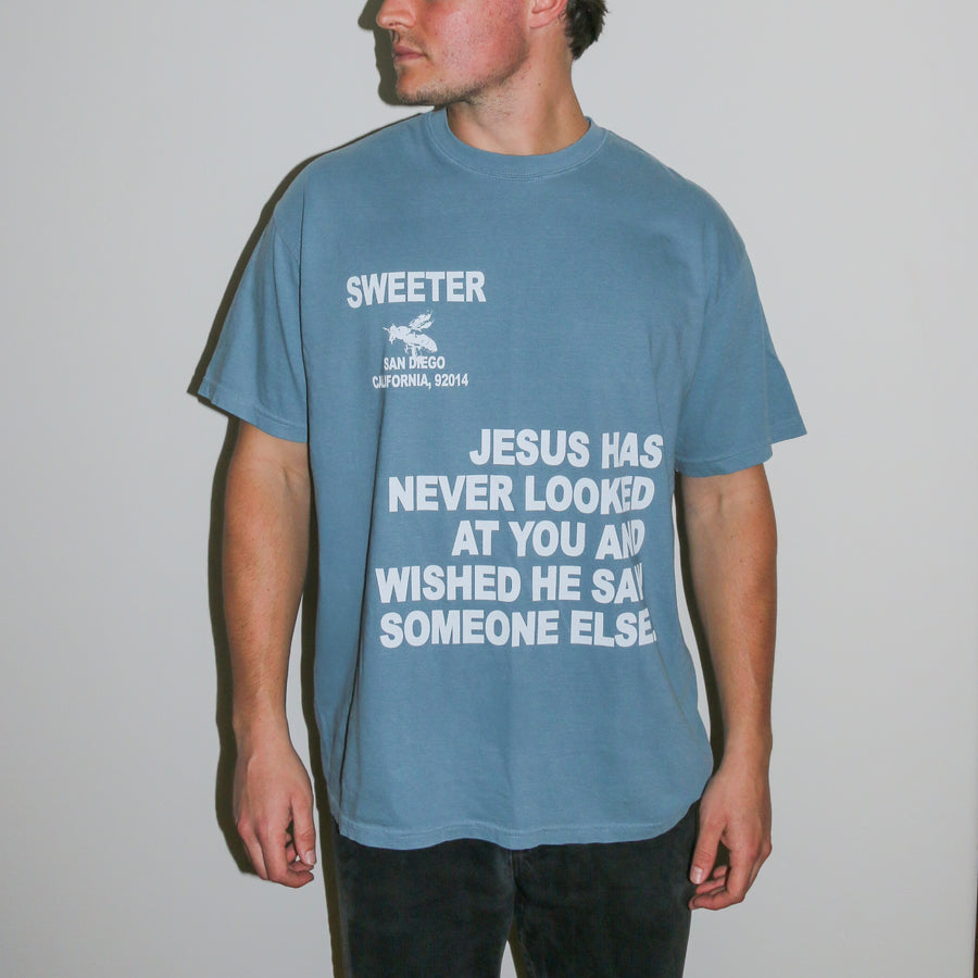 A man wearing a dusty blue graphic t-shirt with white text that reads 'SWEETER SAN DIEGO CALIFORNIA 2014' and 'JESUS HAS NEVER LOOKED AT YOU AND WISHED HE SAID SOMEONE ELSE'.
