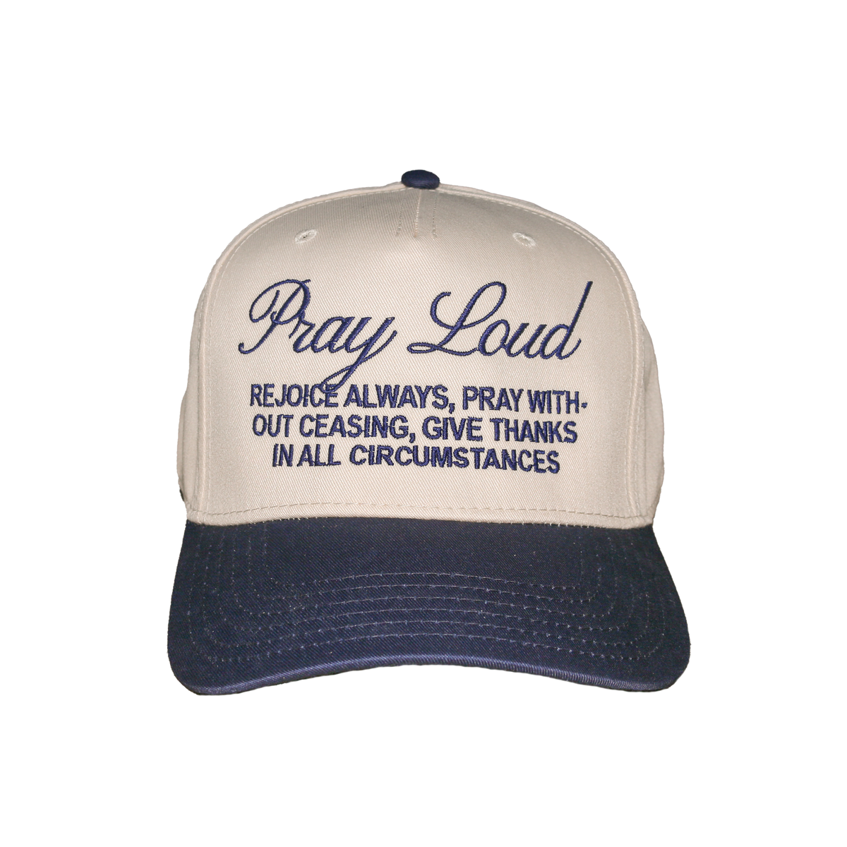 A baseball cap with a cream-colored crown and a navy blue brim, featuring embroidered text on the front that reads 'Pray Loud' and 'REJOICE ALWAYS, PRAY WITHOUT CEASING, GIVE THANKS IN ALL CIRCUMSTANCES'.
