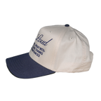A baseball cap with an off-white crown and a navy blue brim, featuring navy blue embroidered text on the front that reads 'Loud' and 'pray with thanksgiving'.