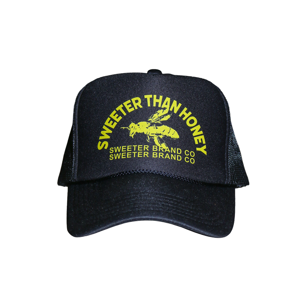 A black trucker-style cap with yellow embroidered text reading 'SWEETER THAN HONEY' and 'SWEETER BRAND CO' around a bee graphic on the front, shown on a plain white background.