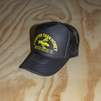 A black trucker hat with yellow embroidered text and a bee graphic reading 'SWEETER THAN HONEY' and 'SWEETIER BRAND CO', placed on a light wood surface.