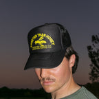 A man wearing a black trucker hat with yellow embroidered text reading 'SWEETER THAN HONEY' and 'SWEETER BRAND CO' on the front, photographed outdoors against a dusk sky.