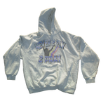 A light gray heather pullover hoodie featuring a front graphic with the text 'NEVER 2 FLY 2 PRAY' in blue and purple outlined lettering, with a black silhouette of a person praying and a small rainbow accent.