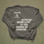 A dark gray crewneck sweatshirt with white printed text and a small graphic, laid flat on a textured gray concrete surface. The text reads 'SWEETER SAN DIEGO CALIFORNIA, 52014' and 'JESUS HAS NEVER LOOKED AT YOU WISHED HE WISHED HE Someone else.